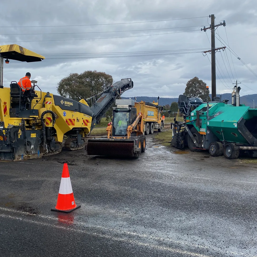 A machine is working on a road with cones in the background.