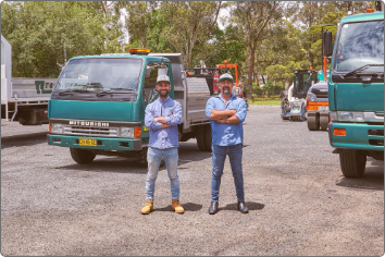 Two men standing in front of two trucks.